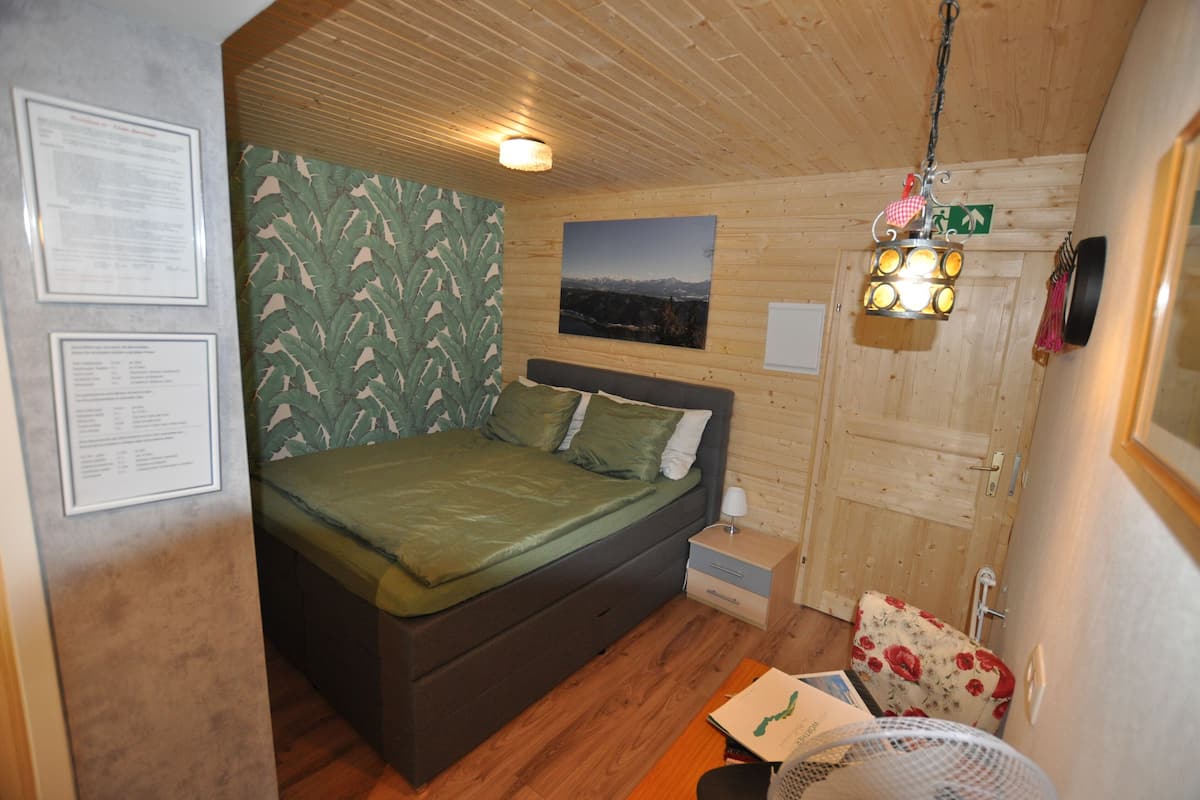 Ein holzgetäfeltes Zimmer im Blockhausstil mit einem Bett, einem Nachttisch, einer Lampe, einem Bild an der Wand und einer Holzbalkendecke.