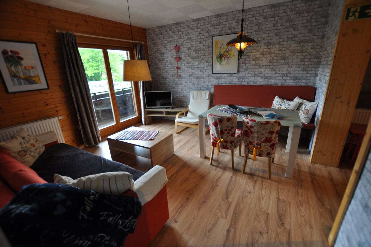 Ein gemütliches Zimmer mit Bett, Schreibtisch, Stuhl, Lampe und Laptop.