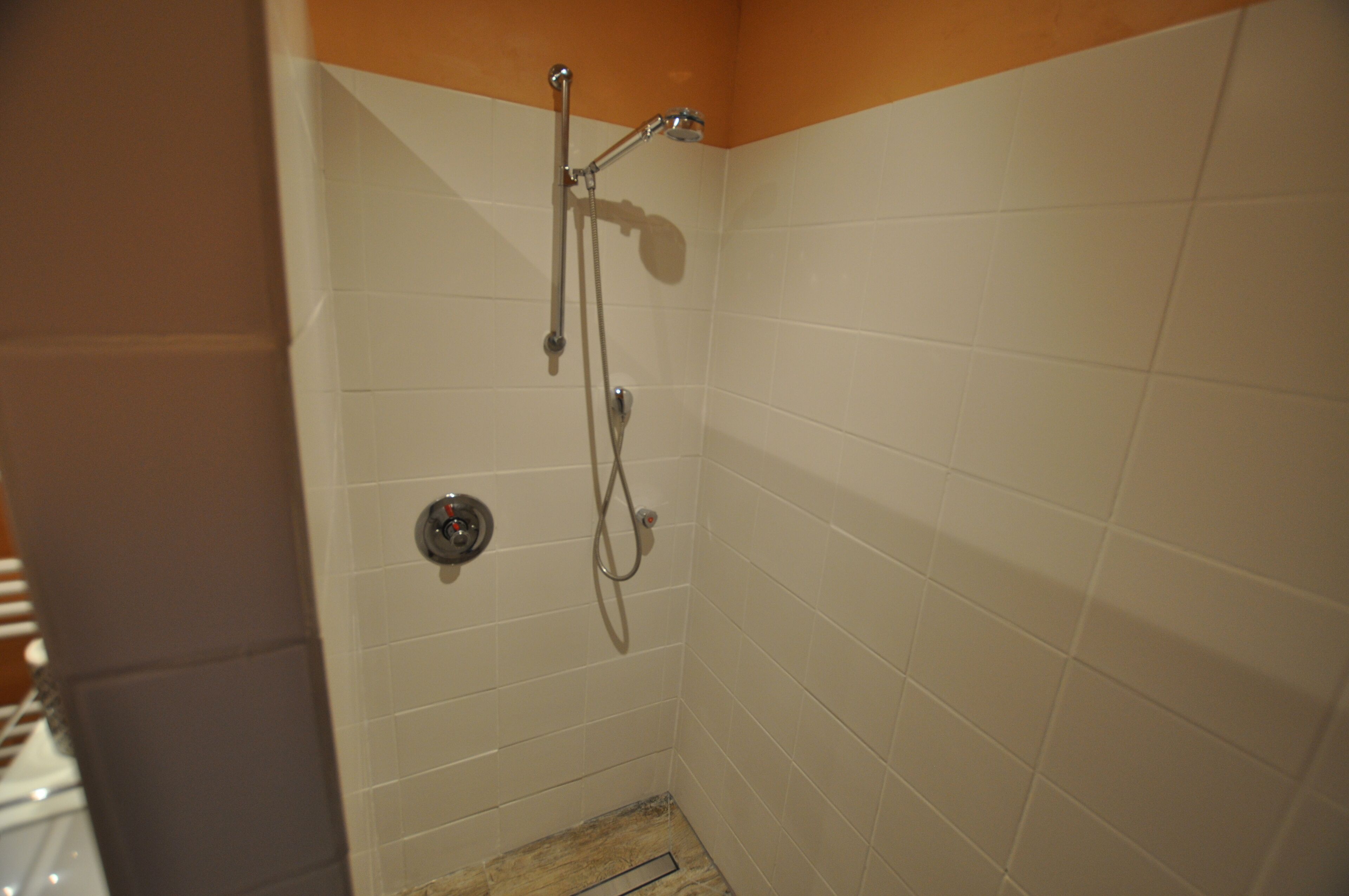 A small, tiled shower area with a handheld showerhead and a wall-mounted faucet.