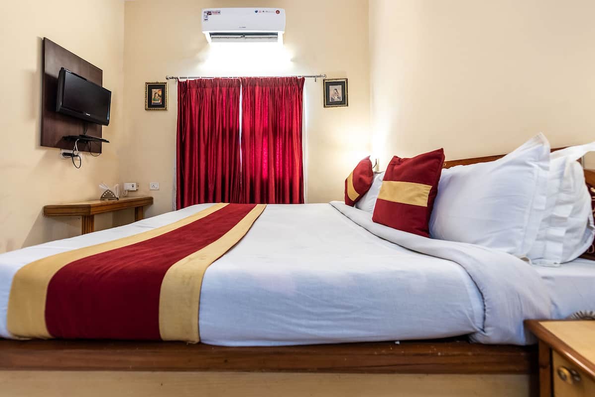Una habitación de hotel con una cama grande, cortinas rojas, un televisor montado y un equipo de aire acondicionado.