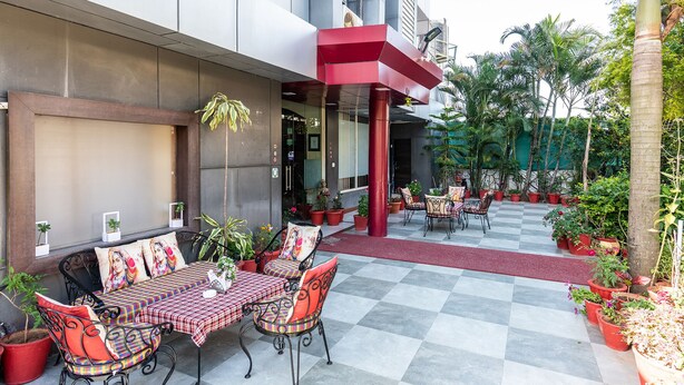 An outdoor seating area with checkered tablecloths and metal chairs, surrounded by potted plants and a red awning. - Yorkshire inn (Abu Road)