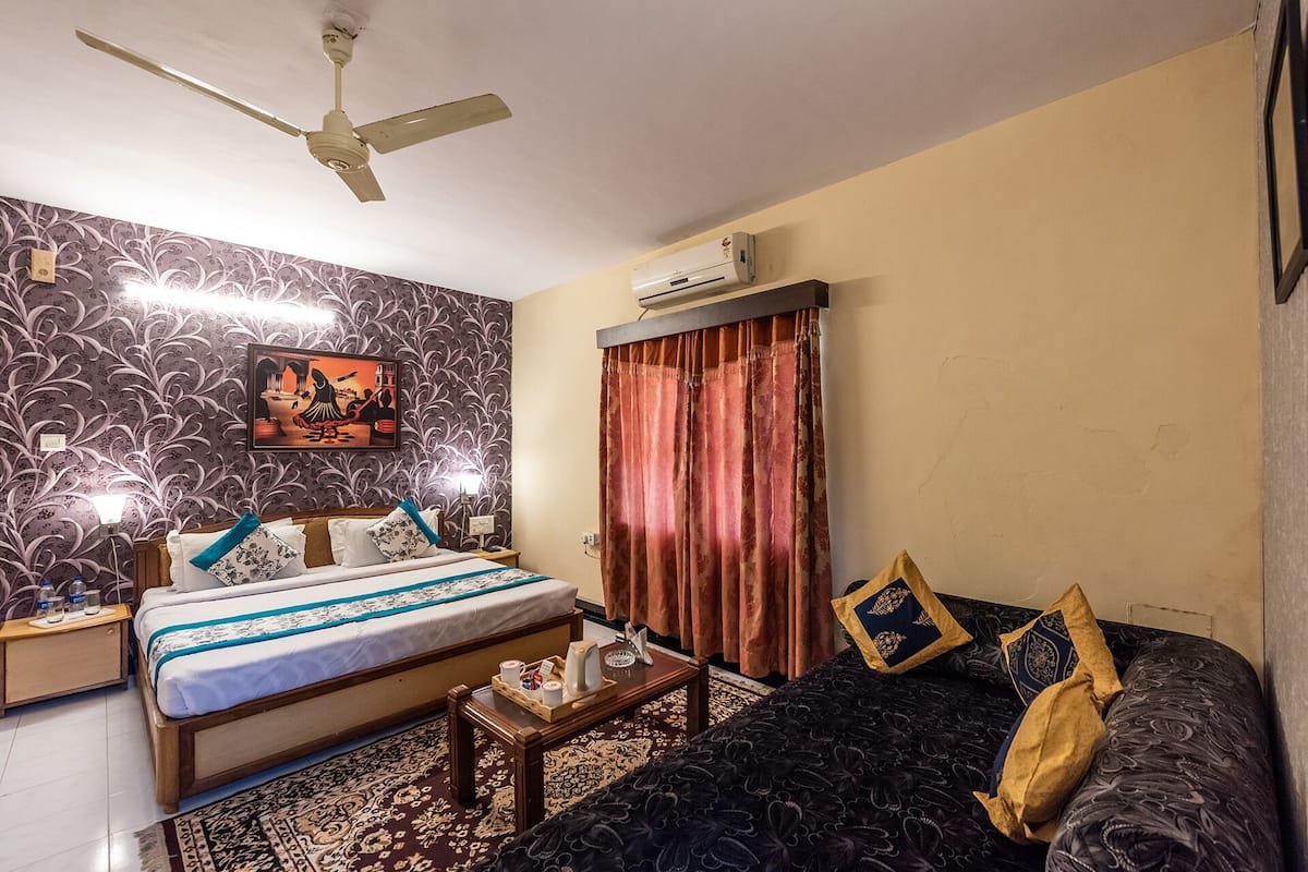 Habitación de hotel con cama, sofá, ventilador de techo, aire acondicionado, pared con estampado y un cuadro.