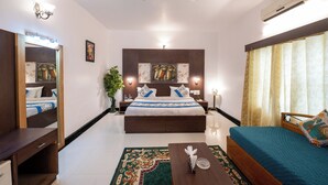A hotel room with a bed, bedside tables, a desk, a mirror, a ceiling fan, and an air conditioning unit. - Yorkshire inn (Abu Road)