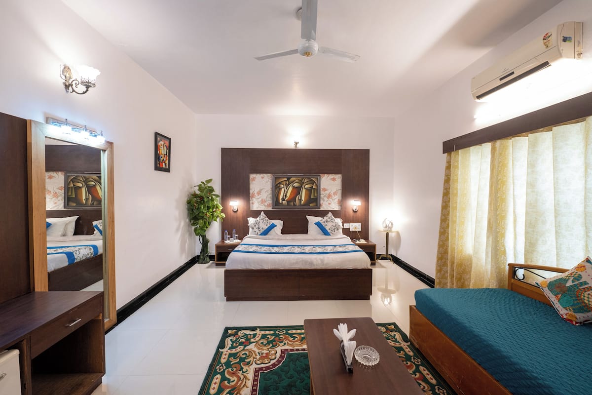 Habitación de hotel con cama, mesitas de noche, escritorio, espejo, ventilador de techo y aire acondicionado.