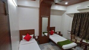 A hotel room with two single beds, a wooden ceiling, a mirror, a small table, and a chair. - Hotel City Palace (Nashik)