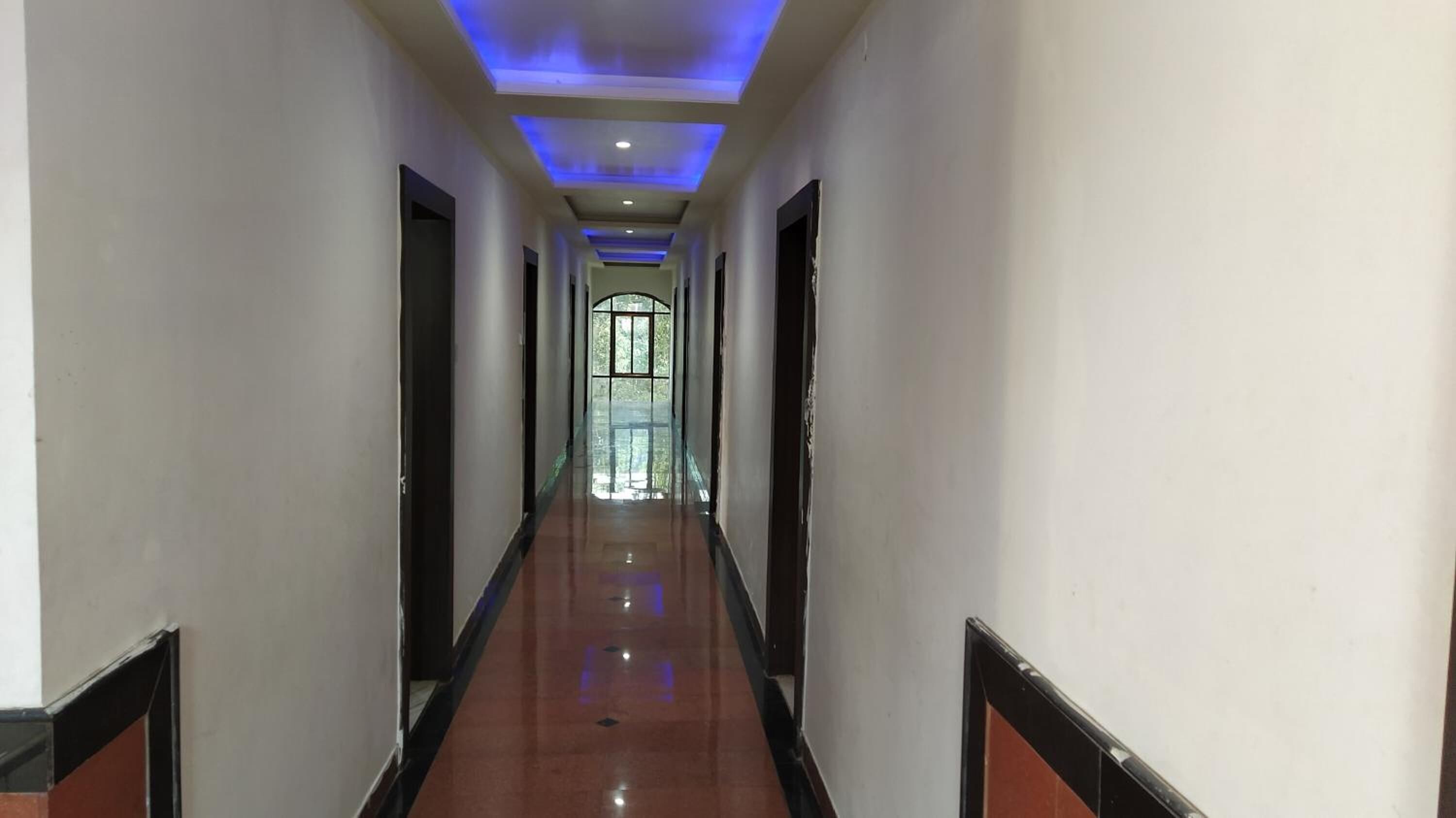 A long, narrow hallway with a polished floor, recessed lighting, and a large window at the end.