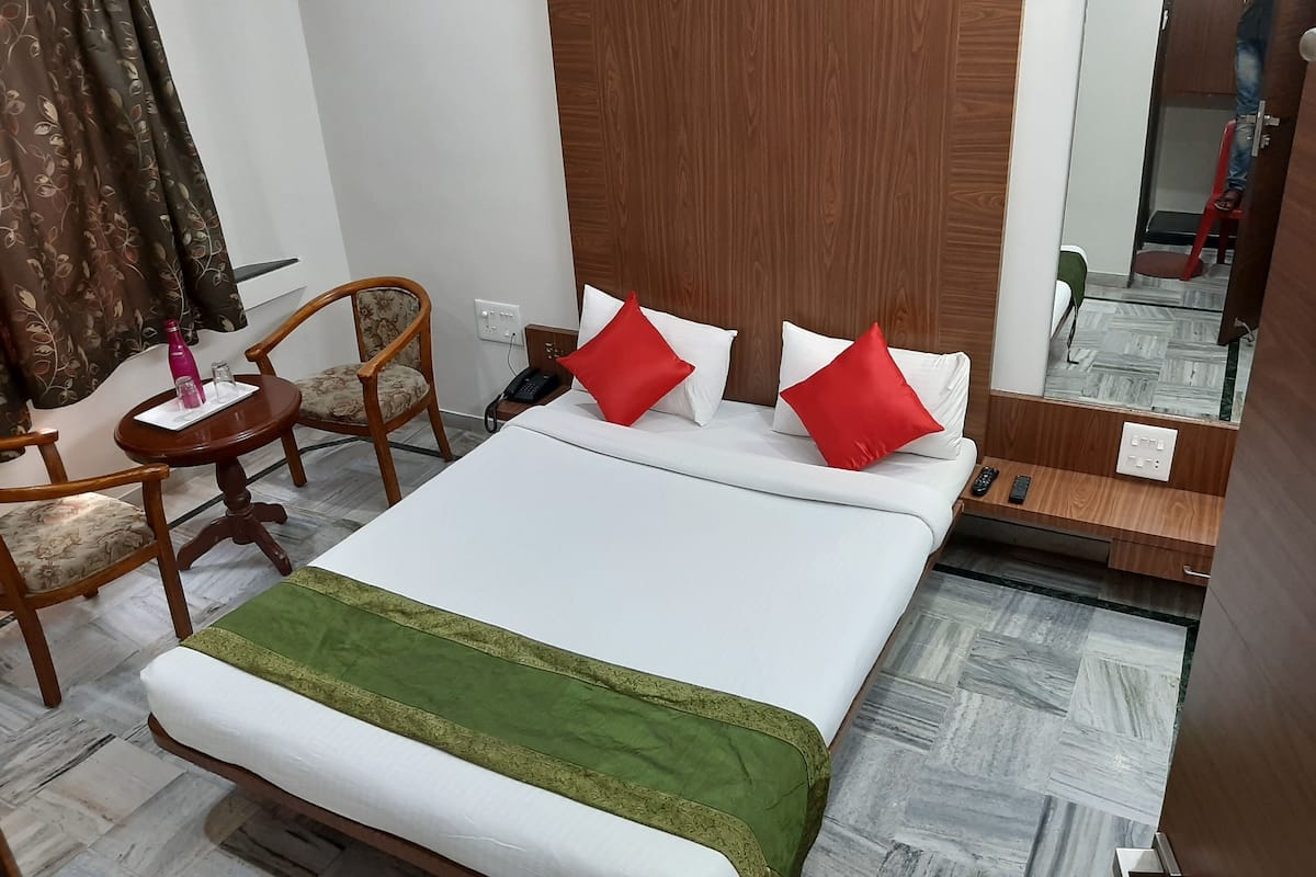 Una habitación de hotel con cama, una silla, una mesita, un espejo y un armario de madera.