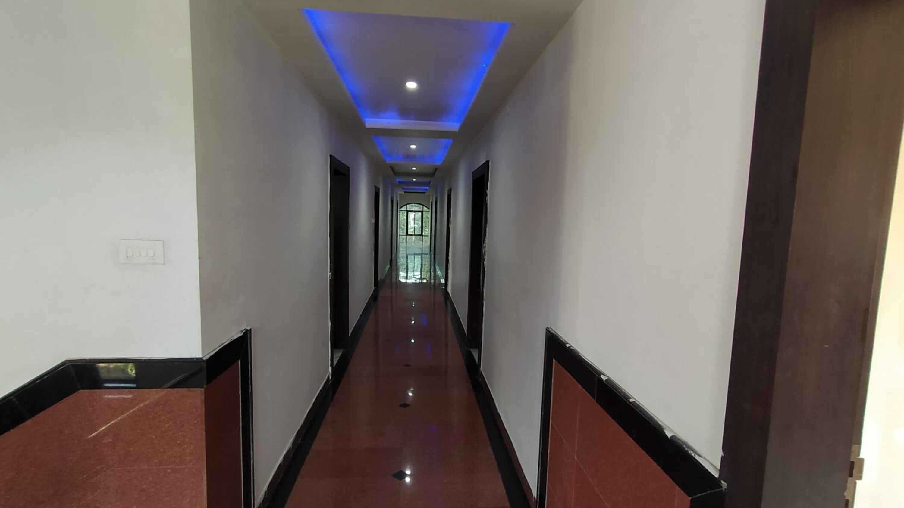 A long, narrow hallway with a reflective floor, recessed lighting, and a door at the end.