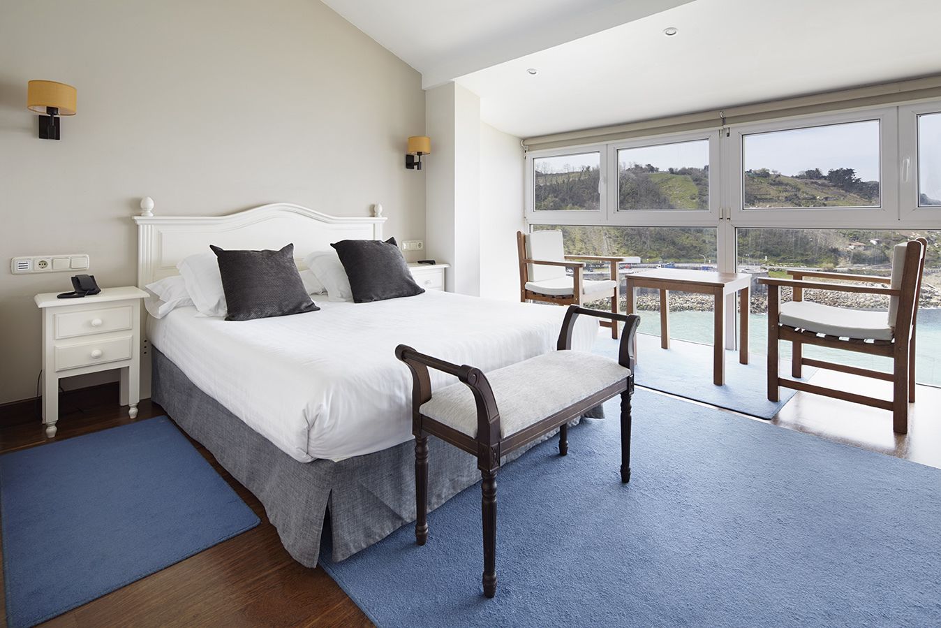A bedroom with a large bed, bedside tables, a chair, and a view of the outdoors.