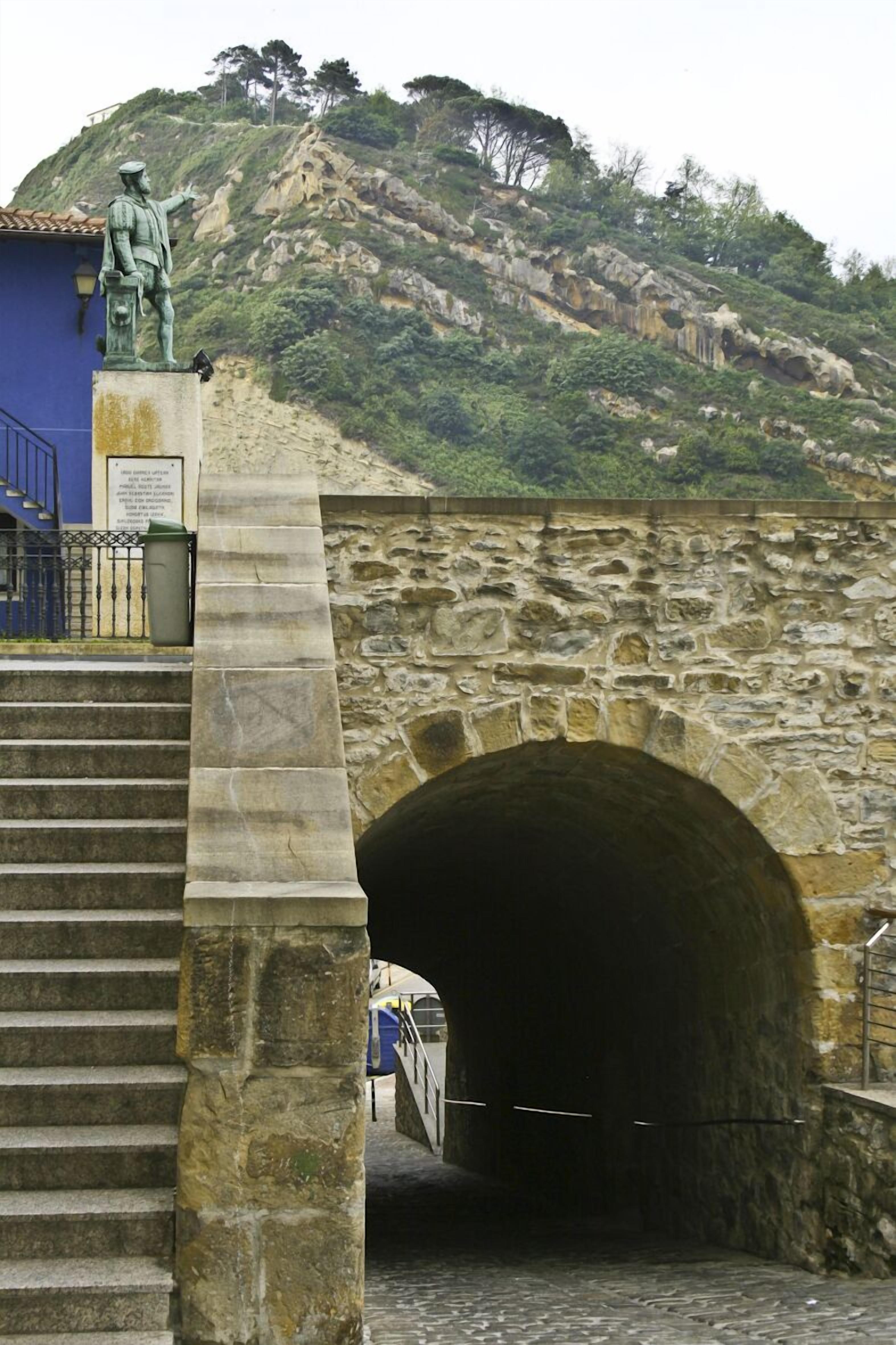 Un puente de piedra con una estatua en la cima que conduce a la entrada de un túnel.