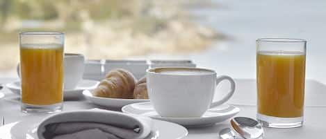 A breakfast setting with croissants, coffee, and orange juice on a table with a scenic view.