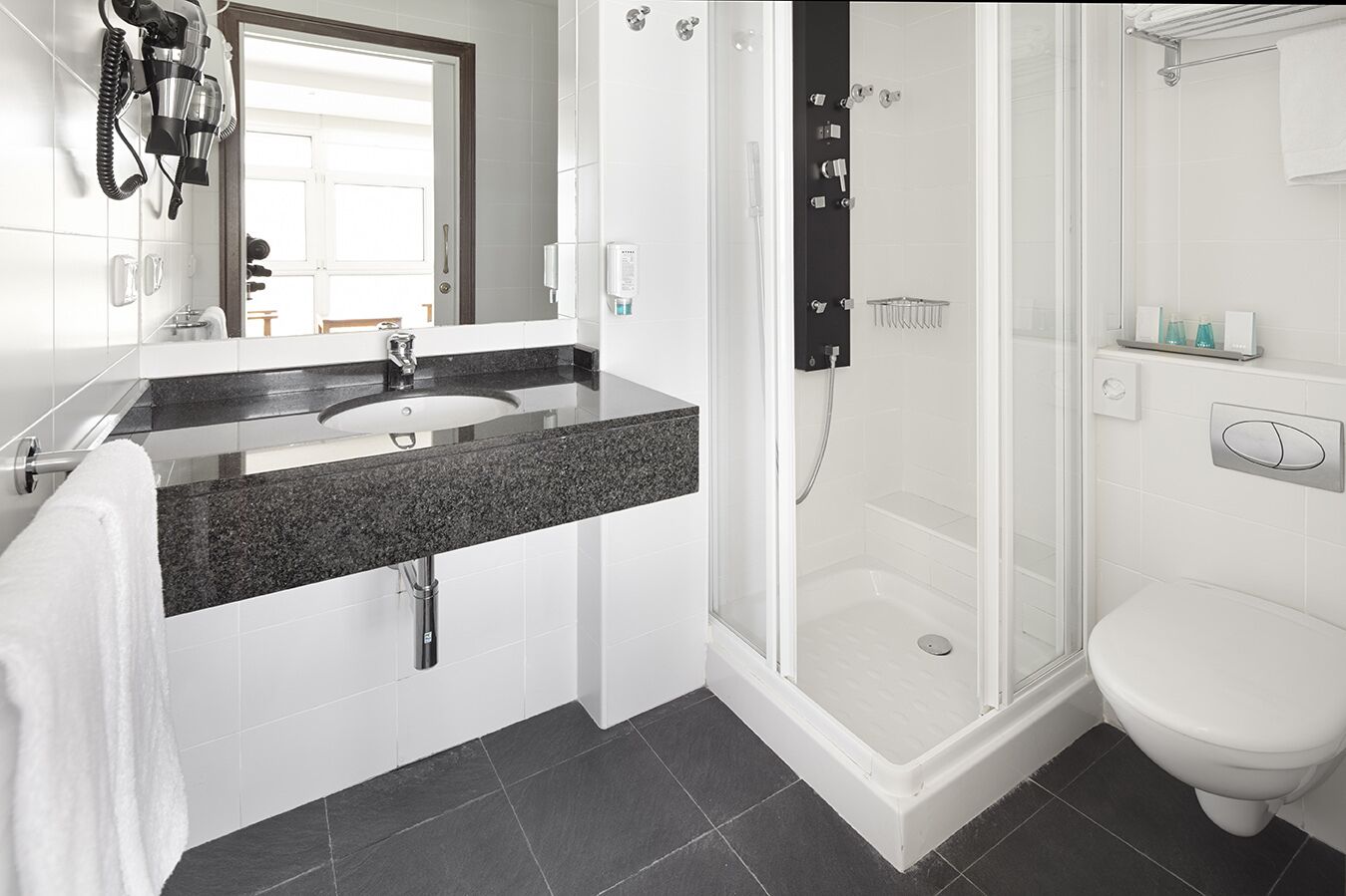 A modern bathroom with a granite countertop sink, a glass-enclosed shower, and a white toilet.