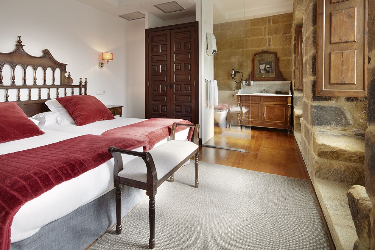 Un dormitorio con dos camas, un cabecero de madera, una mesita de noche, un baño con pared de piedra y un armario de madera.