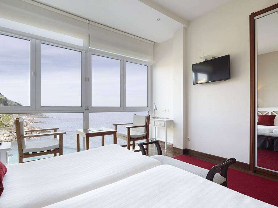 A hotel room with a large window, a bed, a desk, a chair, and a TV.
