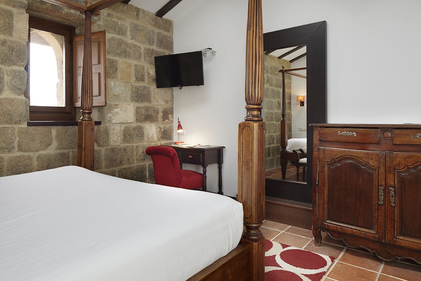 Un dormitorio con pared de piedra, cama, escritorio con silla, televisor y armario.