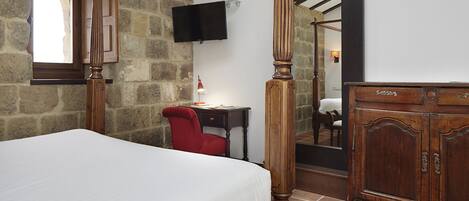 Un dormitorio con pared de piedra, cama, escritorio con silla, televisor y armario.