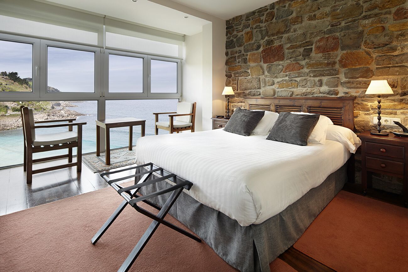 Un dormitorio con una cama grande, pared de piedra y vistas al mar a través de amplios ventanales.