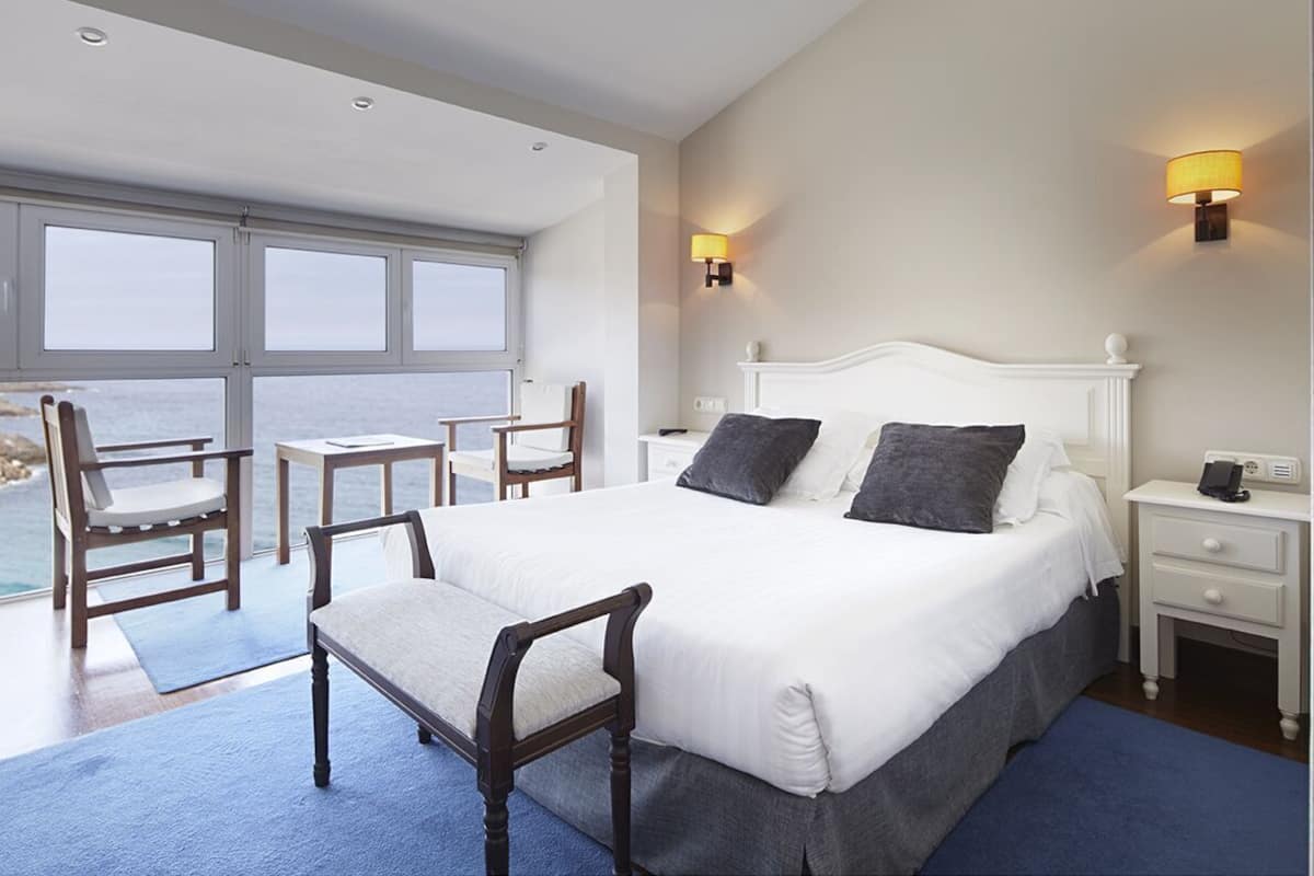 Une chambre d’hôtel avec un grand lit, deux tables de chevet, une chaise, un bureau et une vue sur la mer.