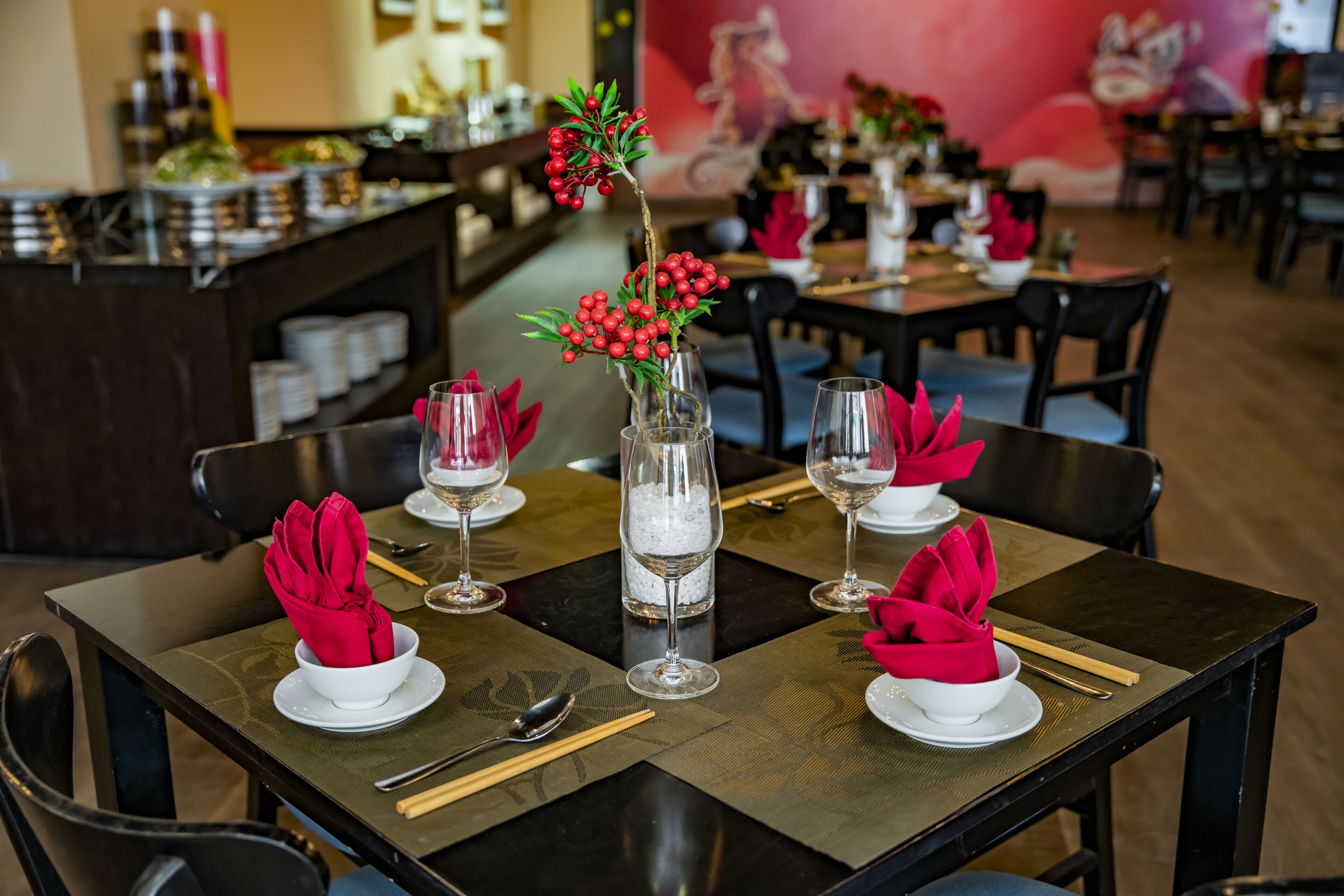 A restaurant setting with tables set for dining, including plates, glasses, and red napkins.