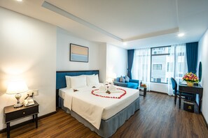 Quarto de hotel com uma cama grande, uma escrivaninha, uma cadeira, um abajur e um telefone em uma mesa de cabeceira.