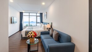 A modern hotel room with a large bed, a blue sofa, a glass coffee table with a vase of flowers, and a view of the sea. - Paralia Hotel Nha Trang (Bac Nha Trang)