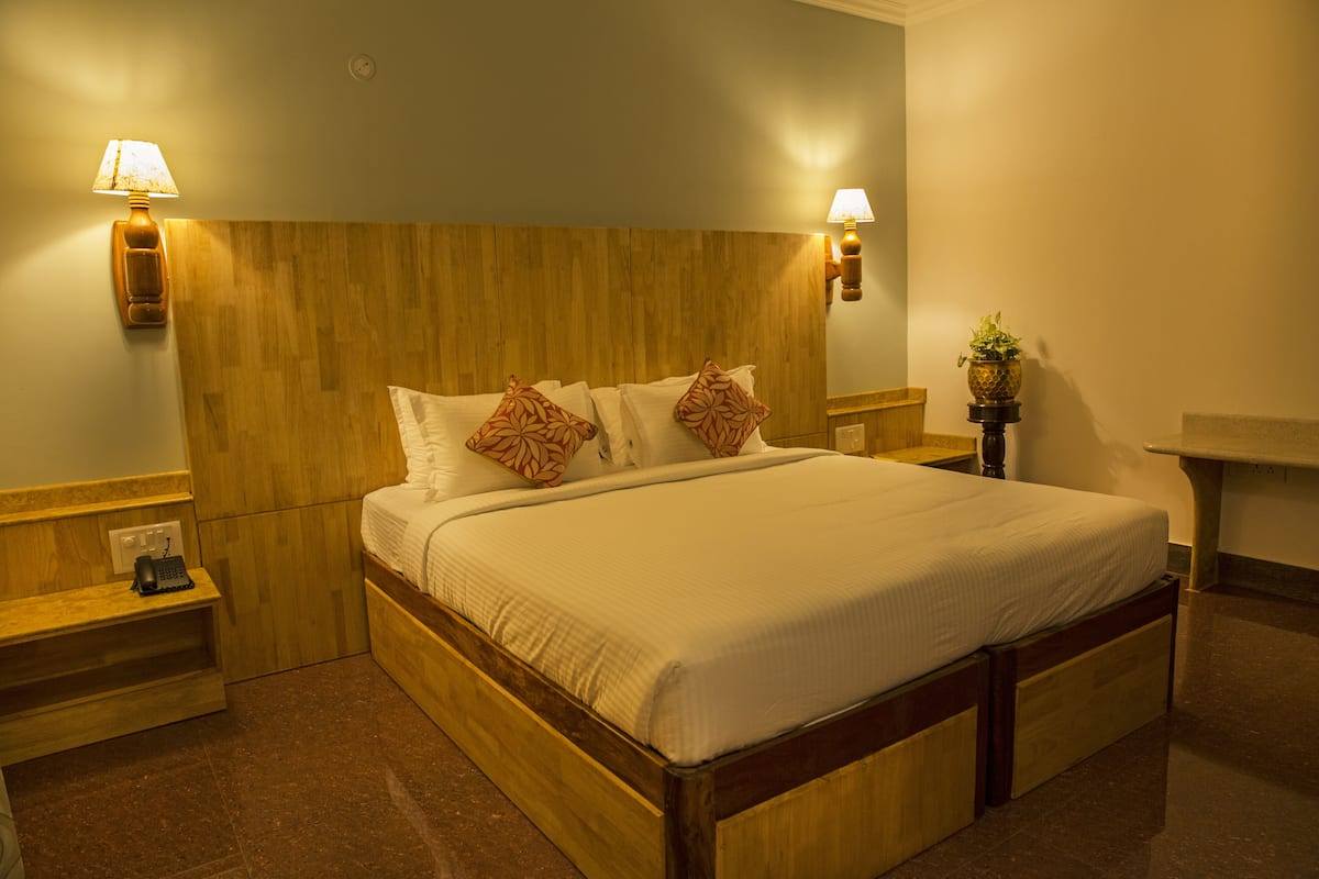 Una cama bien hecha con tablero de madera, dos lámparas de noche y una mesita de noche con un teléfono.