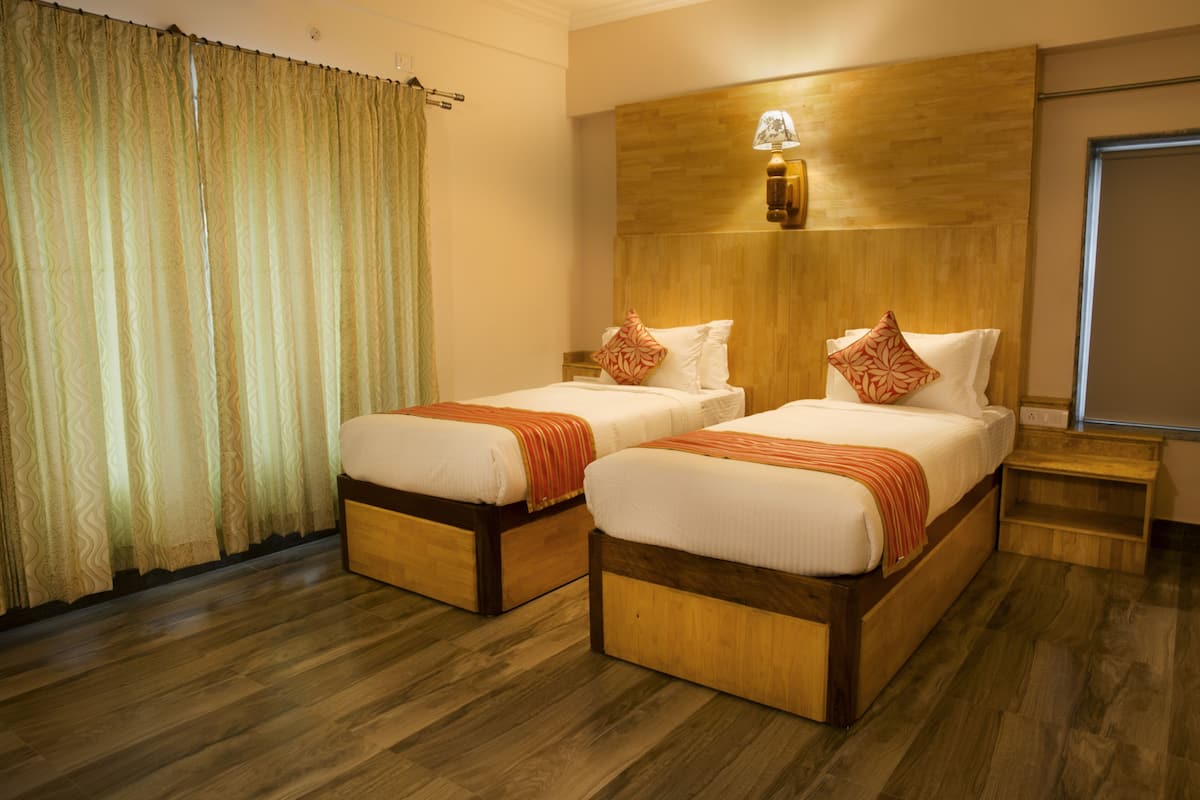 Habitación de hotel con dos camas individuales, cabecero de madera, piso de madera y una ventana con cortinas.