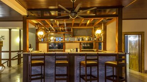Een bar met een marmeren aanrecht, houten krukken en een plafondventilator.