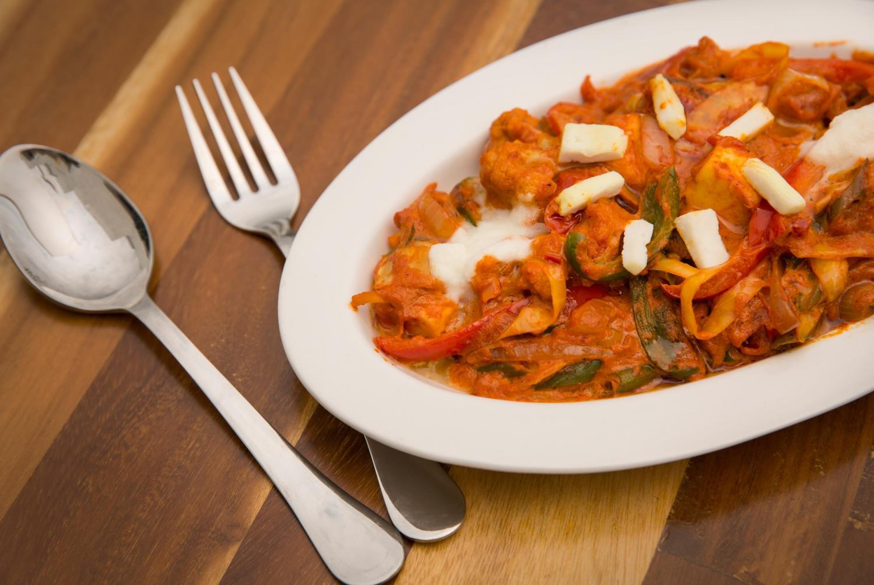 A white plate of food with a fork and spoon on a wooden table.
