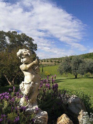 Una estatua de ángel de piedra en un jardín con flores moradas y un cielo despejado.