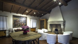 A rustic dining area with a wooden table, white upholstered chairs, a fireplace, and a large painting on the wall. - Costa degli Ulivi (Fumane)