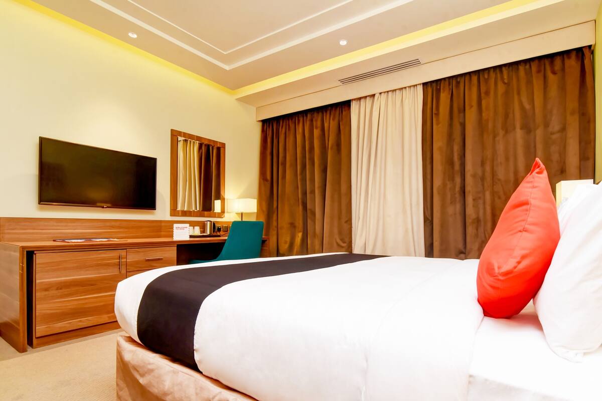 A hotel room with a large bed, a desk, a chair, a TV, and a window with curtains.