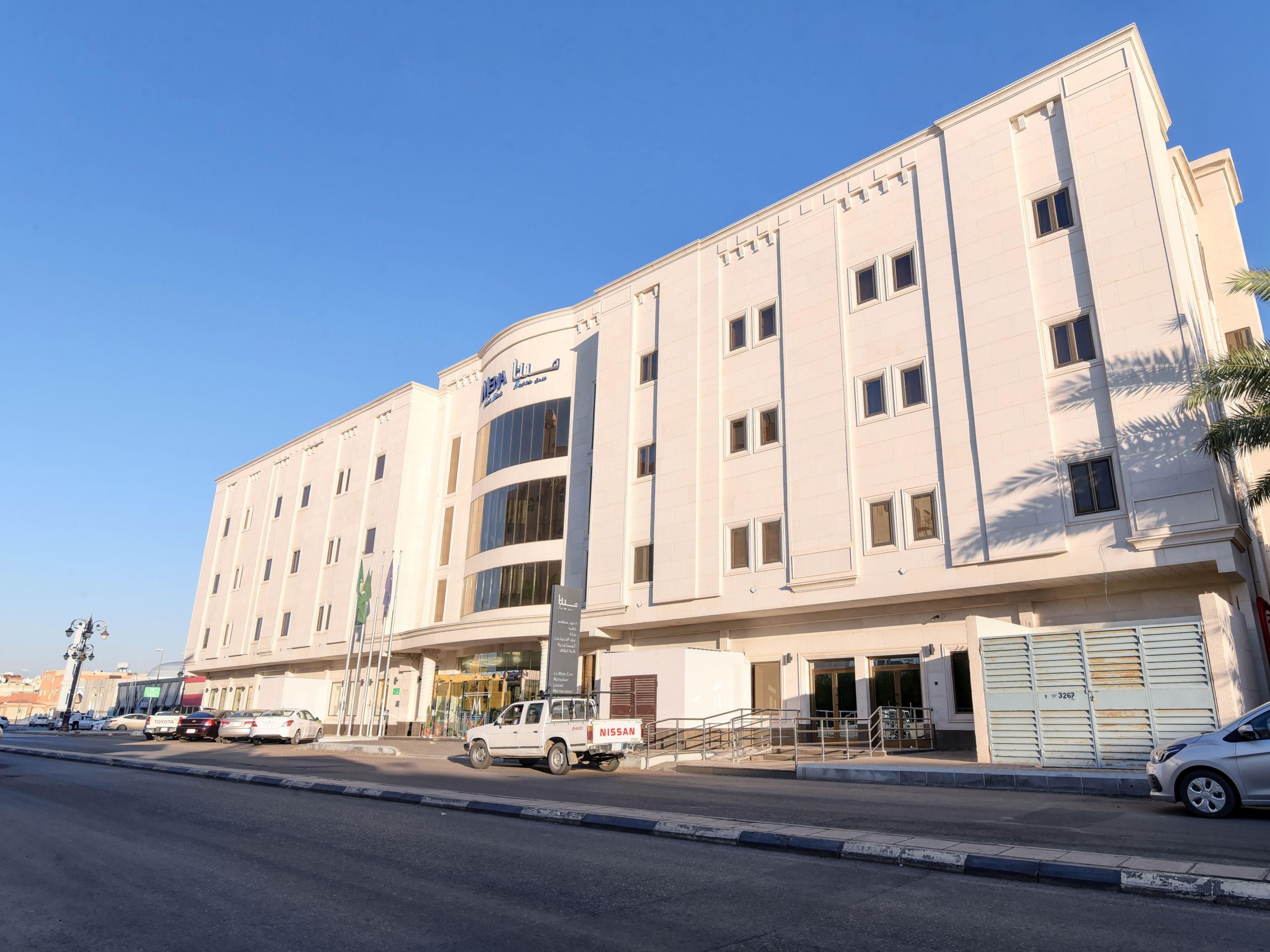 Un edificio de varios pisos con una entrada destacada y una camioneta Nissan estacionada en la parte delantera.