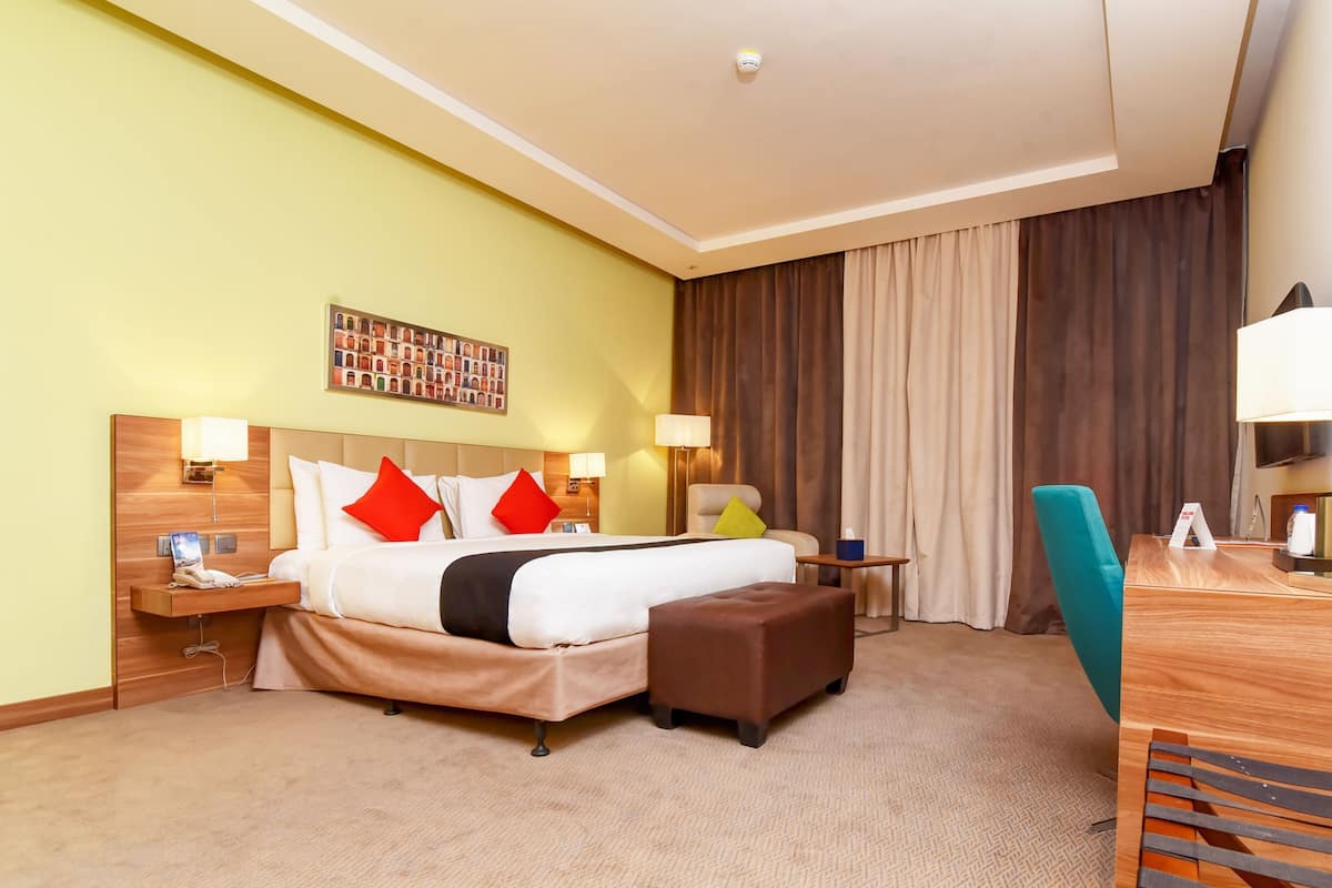 A hotel room with a large bed, bedside tables, a desk, a chair, and a TV.