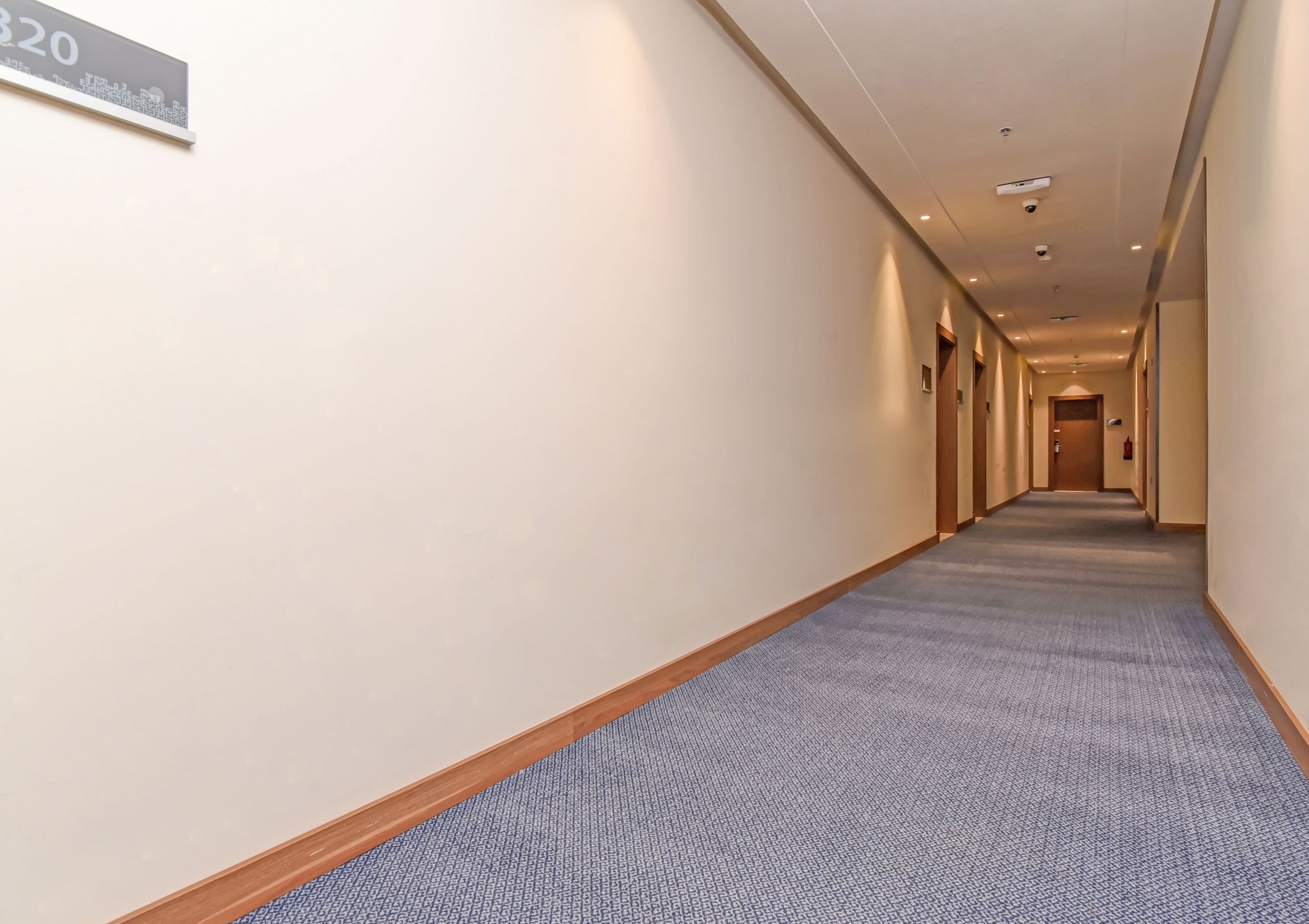 Pasillo de hotel con piso alfombrado, un cartel que indica la habitación 320 y un extintor en la pared.