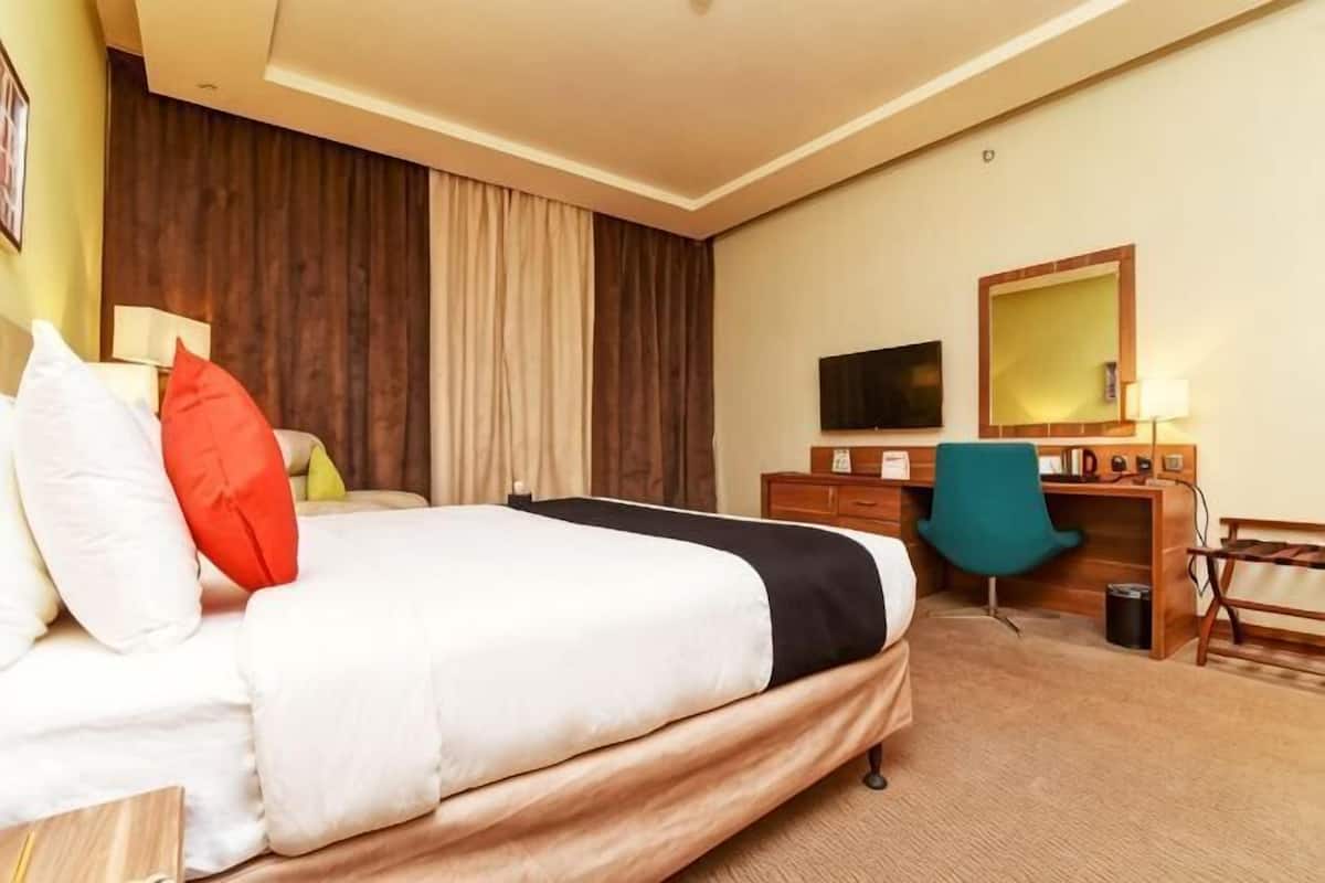 A hotel room with a bed, a desk, a chair, a television, and a mirror.