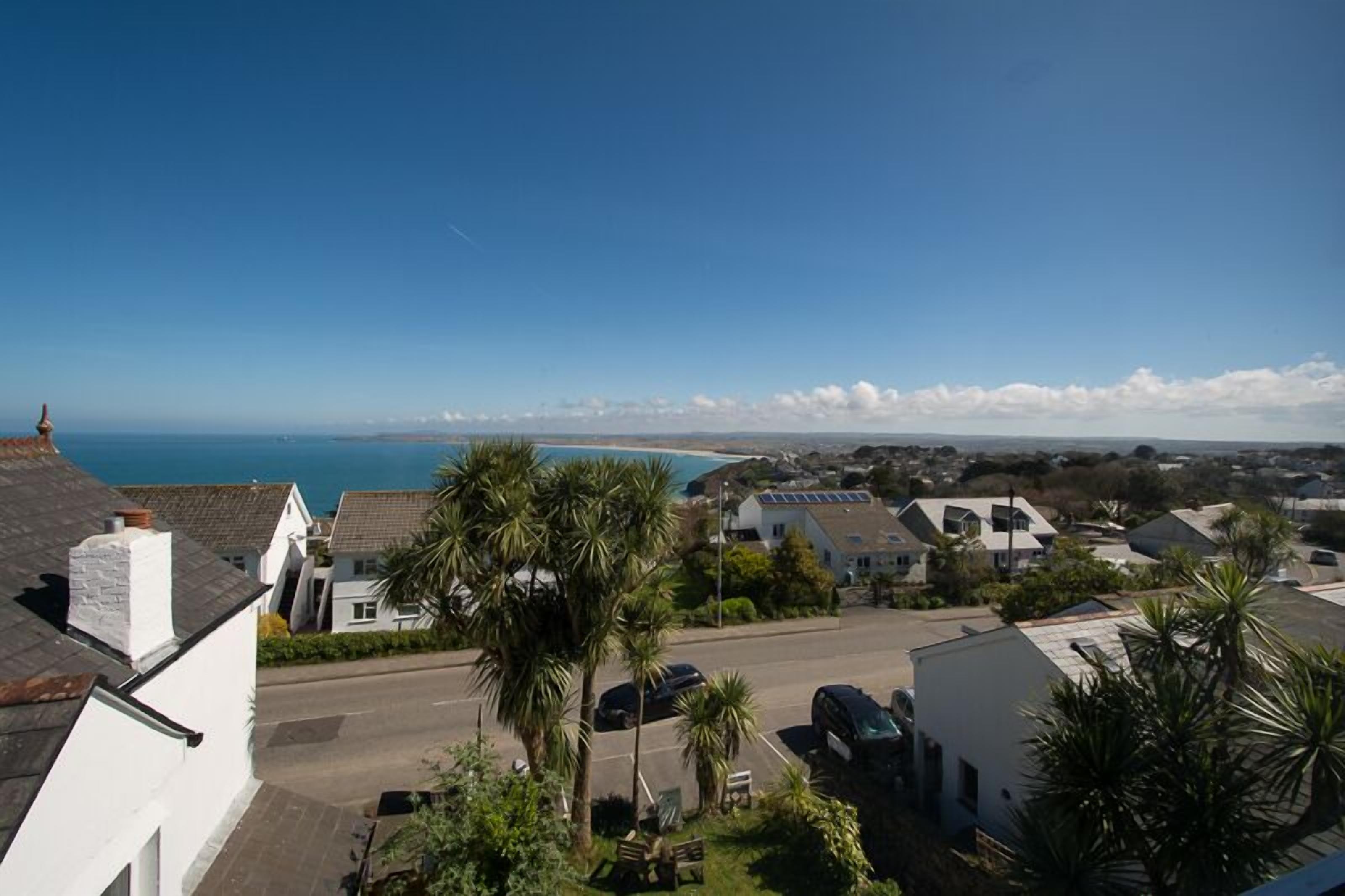 A coastal residential area with houses, a clear sky, and a view of the sea.
