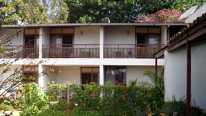 Un edificio de dos pisos con balcones, rodeado de un jardín bien cuidado con diversas plantas y flores.