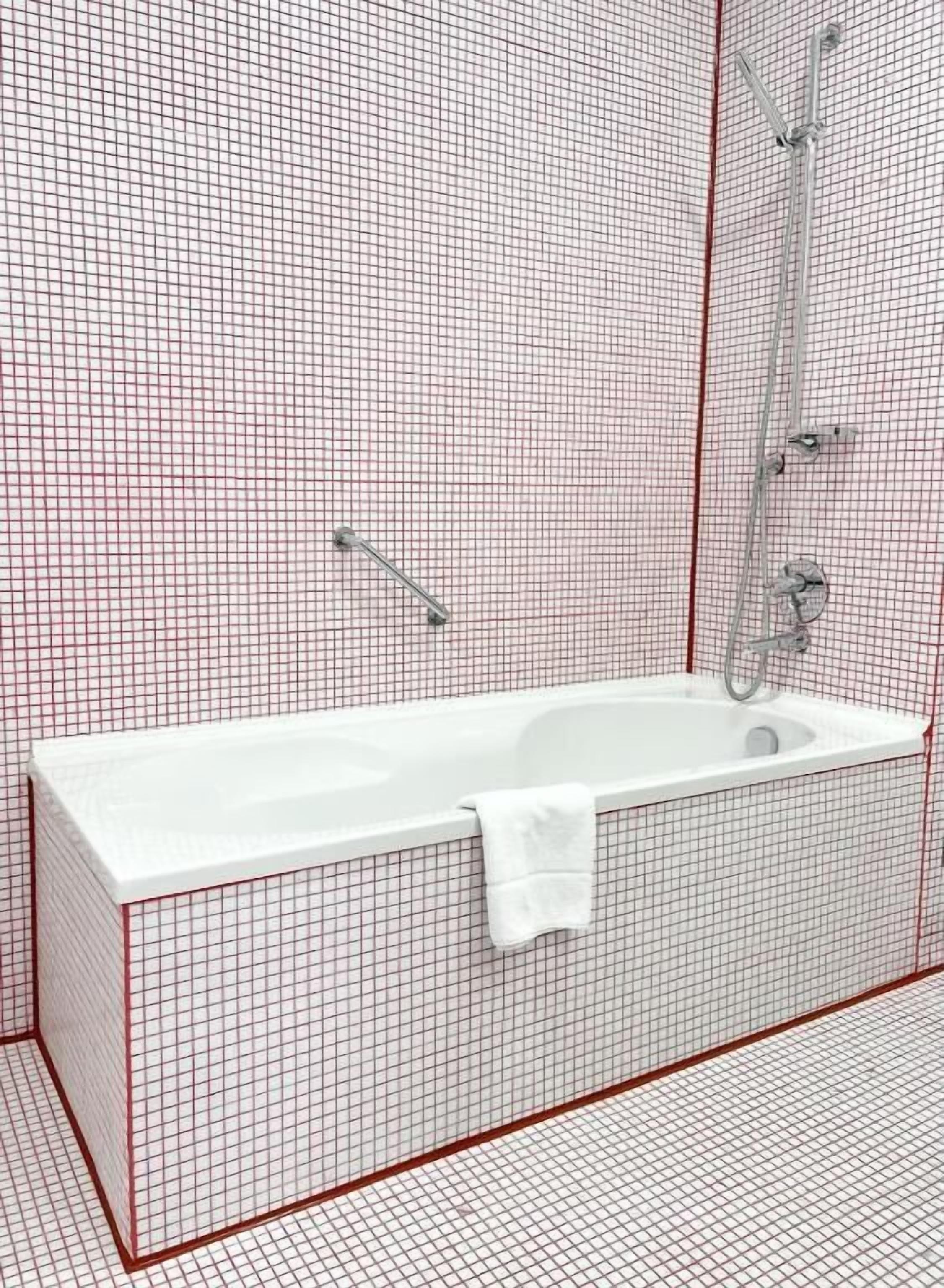 A bathroom with a white bathtub, a shower, and a towel hanging on the side.