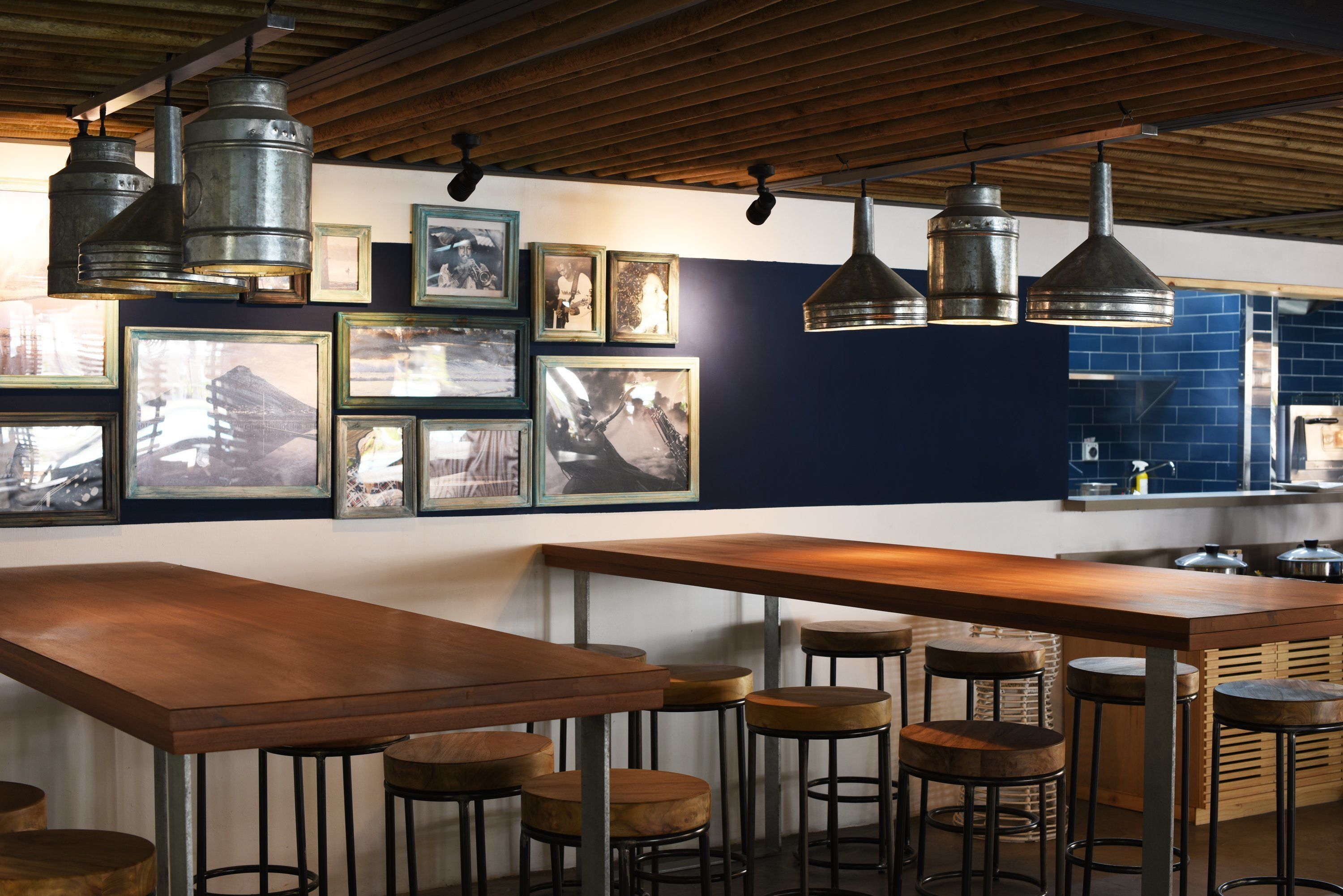 Una zona de bar con mesas y taburetes de madera, cuadros en la pared y lámparas colgantes.