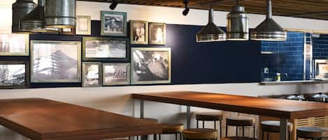 A bar area with wooden tables and stools, framed pictures on the wall, and hanging pendant lights.