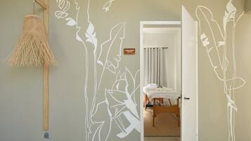 A room with a bed, a hanging rattan lamp, and a wall with a white plant design.