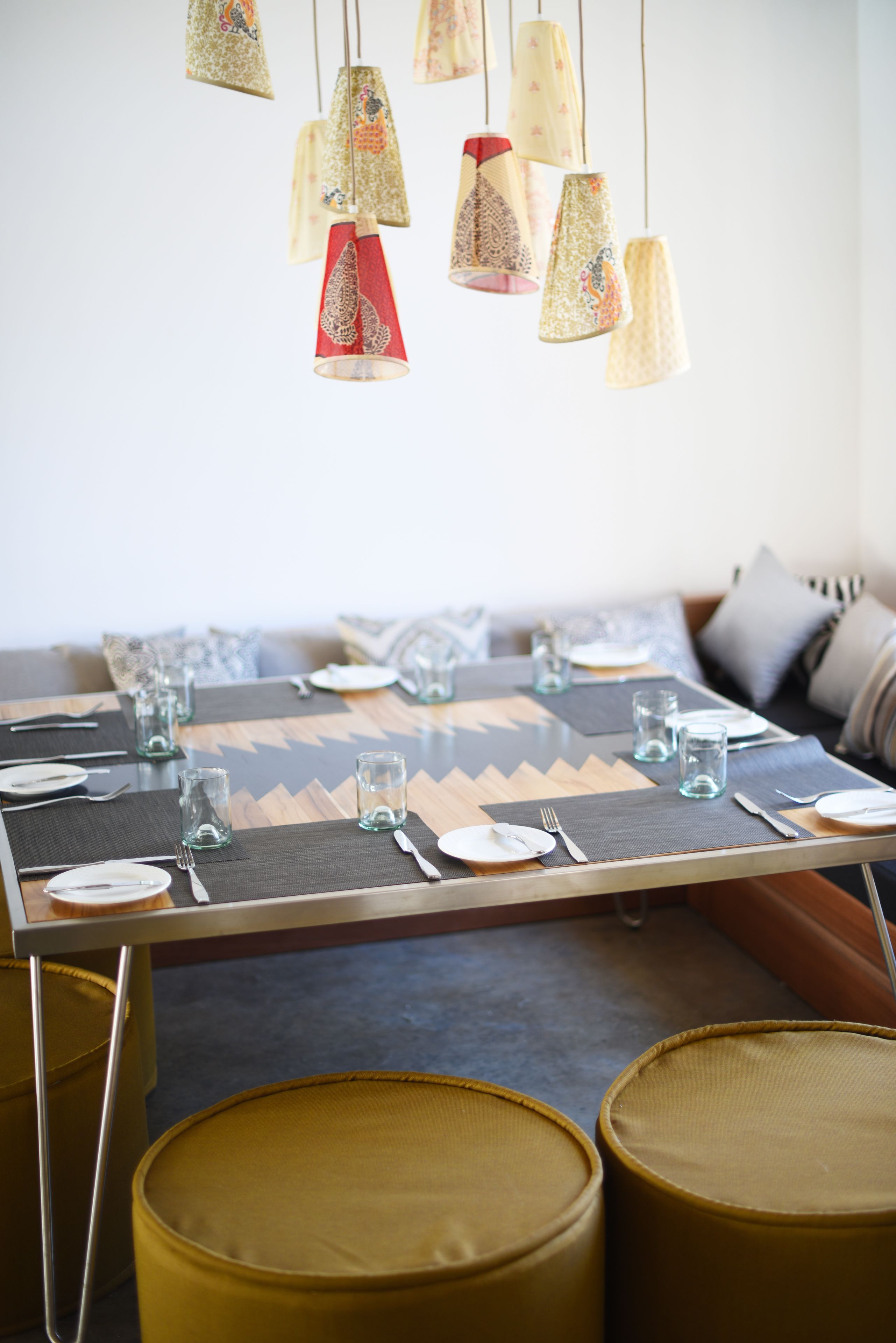 Un comedor con una mesa dispuesta para dos personas, con un mantel decorativo de estampado geométrico, cristalería transparente y varios candelabros con pantallas estampadas.