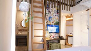 Een slaapkamer met een bed, een bureau met een computer, een ladder en een kleurrijk muurschilderij.
