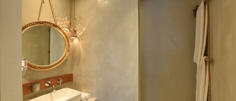Un baño con un lavamanos blanco, un espejo redondo con marco dorado y un perchero para toallas.