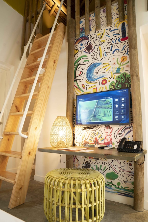A staircase with a wooden handrail, a wall-mounted television displaying a welcome screen, a woven lamp, and a telephone on a wooden table. - Veranda Tamarin Hotel and Spa (Tamarin)