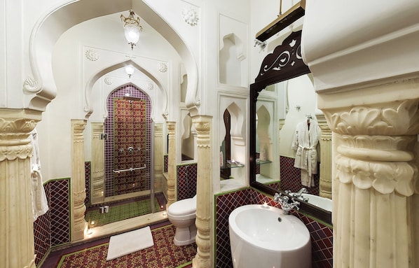 Un baño lujoso con un espejo grande, columnas ornamentales, una bañera y un inodoro.
