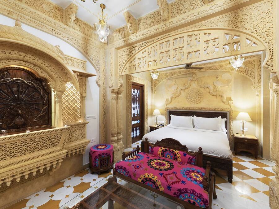 An ornately decorated room with a large bed, intricate wall carvings, and a patterned floor.