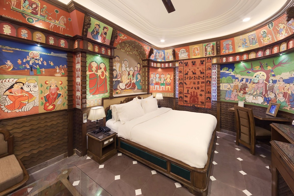 Une pièce comprenant un lit, un bureau et une chaise. Les murs sont décorés de peintures murales colorées.