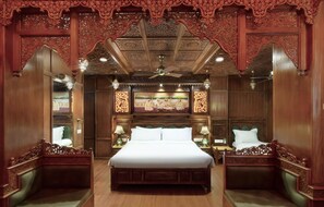 Una habitación tradicional con una cama grande, elaboradas tallas de madera y un ventilador de techo.